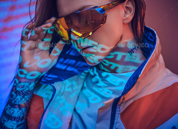 Close up portrait of a young tattooed racer woman posing in a vivid neon studio over text projection - Stock Photo - Images