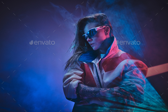 Inked attractive female posing in a neon vivid lights of a studio surrounded by smoke - Stock Photo - Images