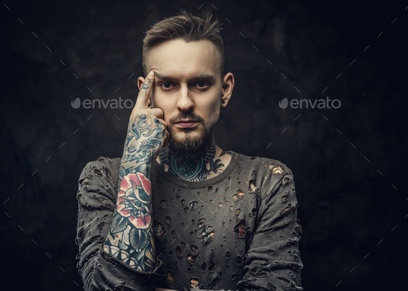 Tattooed male model posing in a dark grey background wearing ripped long-sleeved jumper - Stock Photo - Images