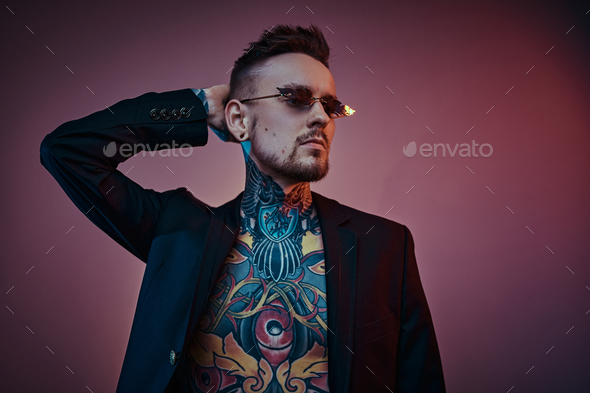 Tattoo artist male model posing in a neon studio with half-naked body, tuxedo and sunglasses. - Stock Photo - Images