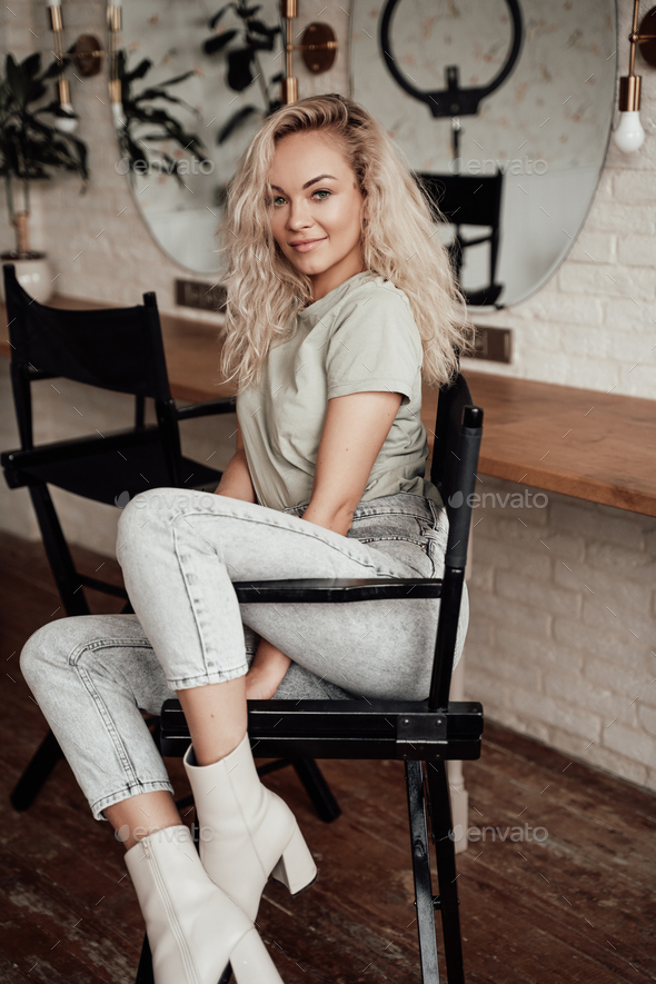Sensual and attractive young woman with curly hair sitting in a bright room on a tall chair - Stock Photo - Images
