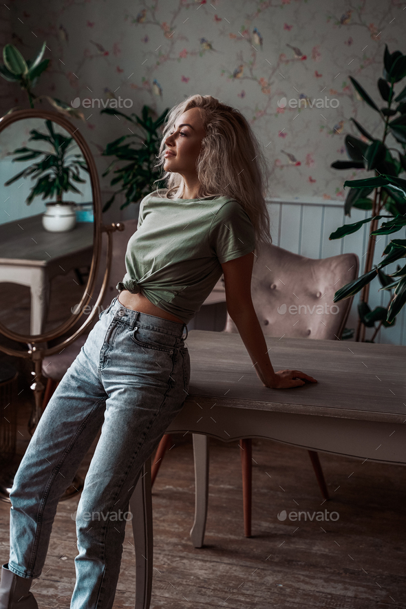 Sensual and attractive young woman with curly hair leaning on table in a bright apartment - Stock Photo - Images