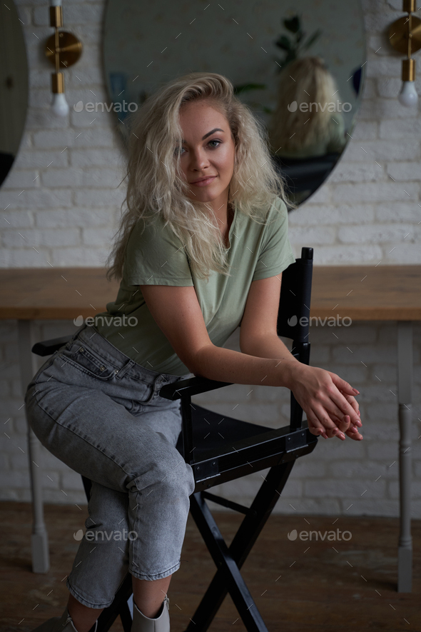 Smiling and cute woman sitting in a make up studio on a tall chair in front of round mirrors