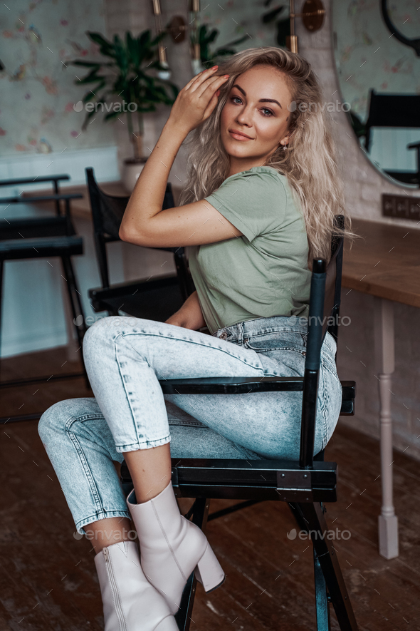 Sensual and attractive young woman with curly hair sitting in a bright room on a tall chair - Stock Photo - Images