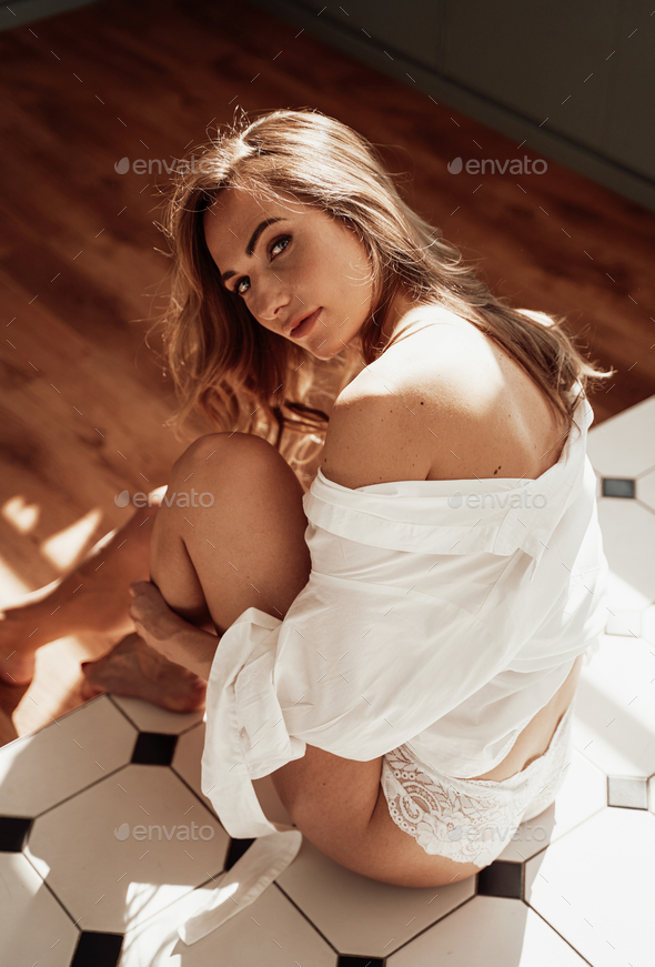 Lovely young woman posing for photoshoot in lingerie and sitting on the tile floor - Stock Photo - Images