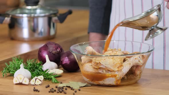 Pour sauce over chicken legs. Chef prepares marinade and stirs raw chicken legs in glass bowl alt