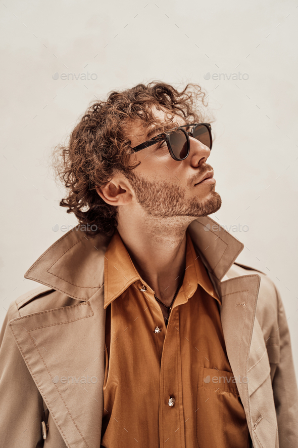 Portrait of a handsome casual guy with curly hair posing in the bright studio - Stock Photo - Images
