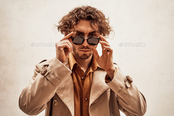 Portrait of a young man with curly hair posing in a bright studio looking vogue - Stock Photo - Images