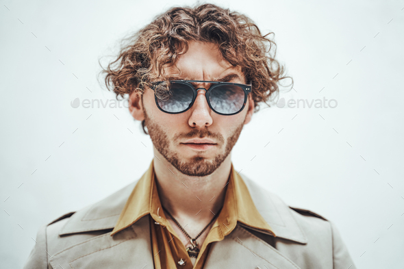 Portrait of a young man with curly hair posing in a bright studio looking vogue - Stock Photo - Images