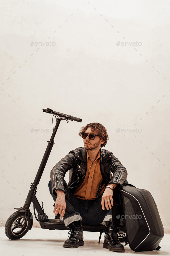 Assertive and rich young man posing on a scooter in a bright studio, looking cool - Stock Photo - Images
