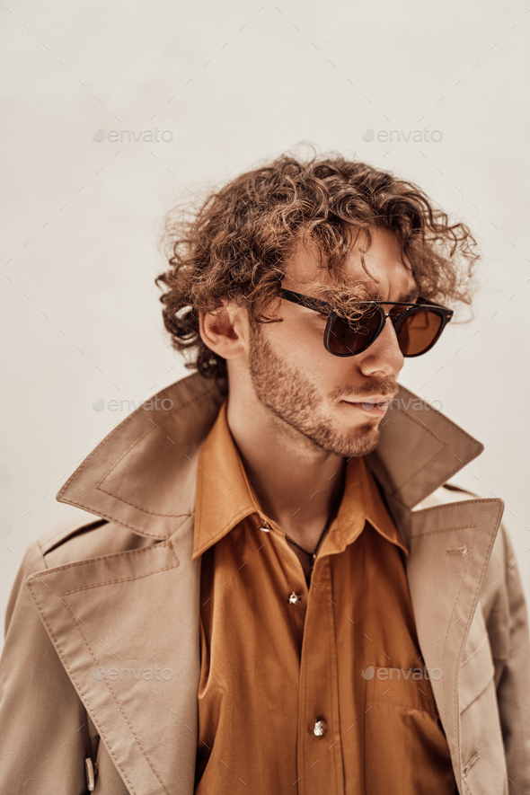 Portrait of a handsome casual guy with curly hair posing in the bright studio - Stock Photo - Images