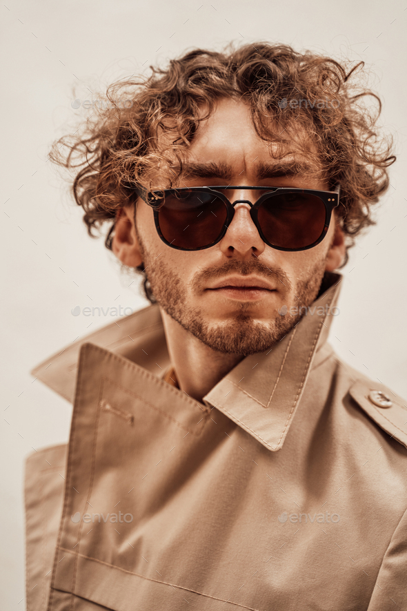 Portrait of a handsome casual guy with curly hair posing in the bright studio - Stock Photo - Images