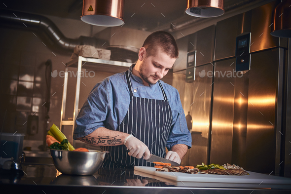 Male chef standing in a restaurant kitchen, cutting vegetables - Stock Photo - Images