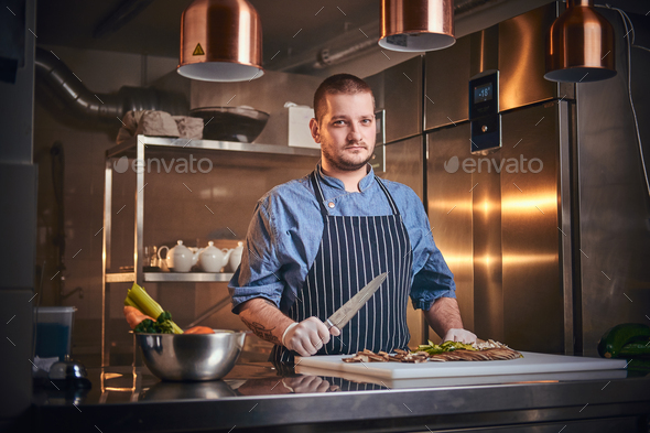 Male chef standing in a restaurant kitchen, holding a knife - Stock Photo - Images