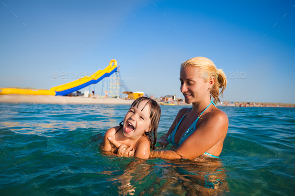 Young mother standing in water and helping to swim her small daughter