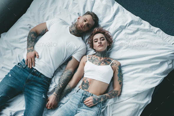 Top View of Young Tattooed Couple Holding Hands and Lying on Bed
