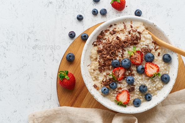 Oatmeal porridge rustic with berries and chocolate, dash diet, on white wooden background top view