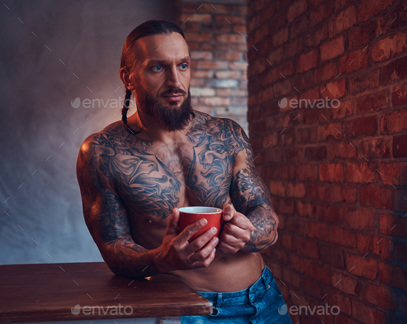 Handsome tattooed man with a stylish haircut and beard standing against a  brick wall Stock Photo by fxquadro