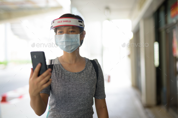 Young Asian woman using phone with mask and face shield for protection from corona virus outbreak in