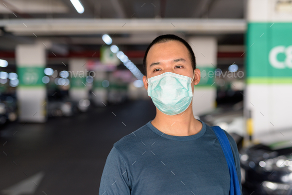 Face of young Asian man with mask thinking at the parking lot