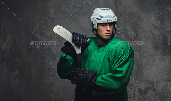 Hockey player wearing black protective uniform holds a hockey stick on a gray background.