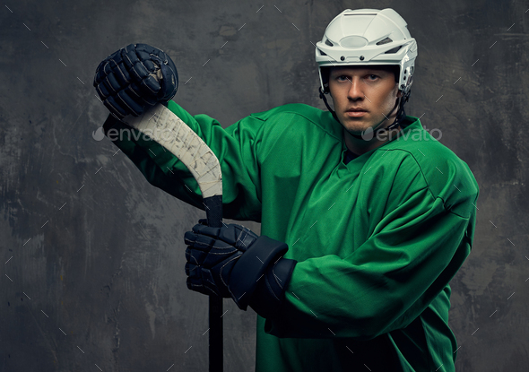 Hockey player wearing black protective uniform holds a hockey stick on a gray background.