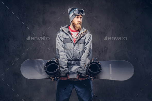 Brutal redhead snowboarder posing with snowboard at a studio. Isolated on the gray background