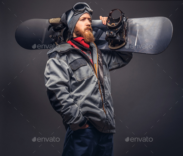 Brutal redhead snowboarder posing with snowboard at a studio. Isolated on the gray background