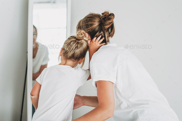 Young mother and daughter in white t-shirts look in mirror