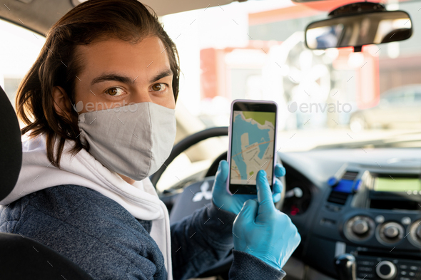 Young taxi driver in protective mask and gloves pointing at smartphone screen