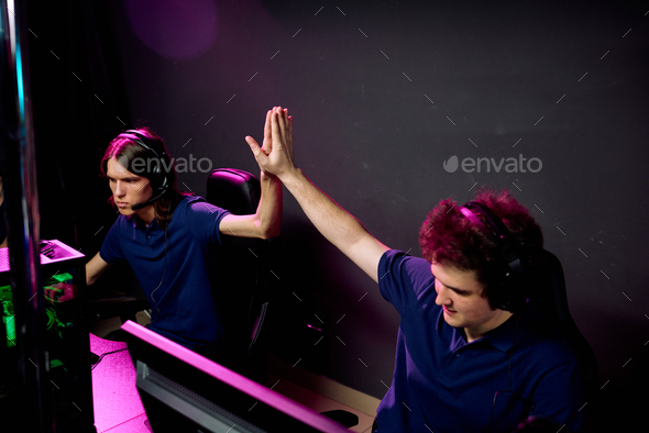 Two guys in headphones giving each other high five while looking at screens
