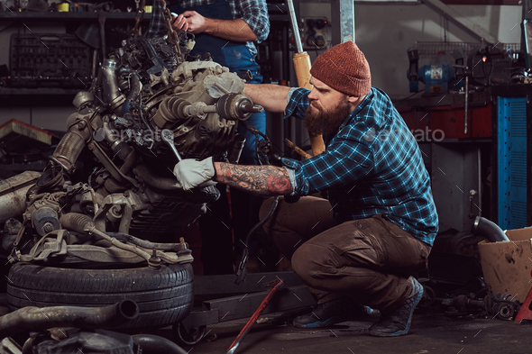 Brutal tattooed mechanic repairs the car engine in the garage. Service station. - Stock Photo - Images