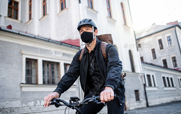 Delivery man courier with face mask and bicycle cycling in town