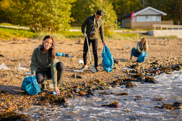 Young woman in a team picking up garbage in bag at beach - Stock Photo - Images