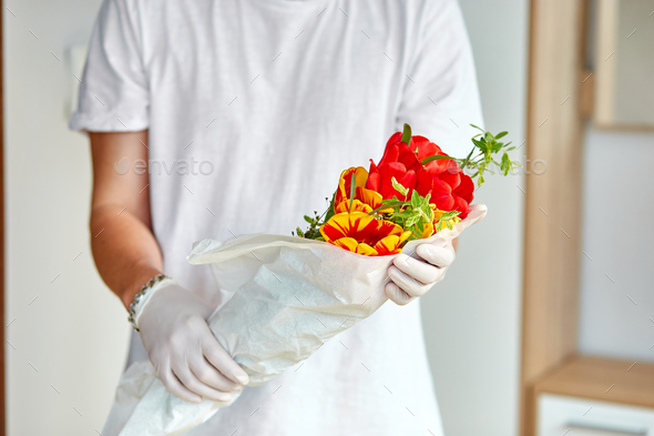 Courier, delivery man in medical latex gloves safely delivers online purchases a bouquet of flower