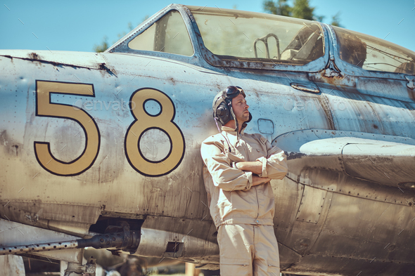 Mechanic in uniform and flying helmet standing near an old war fighter-interceptor