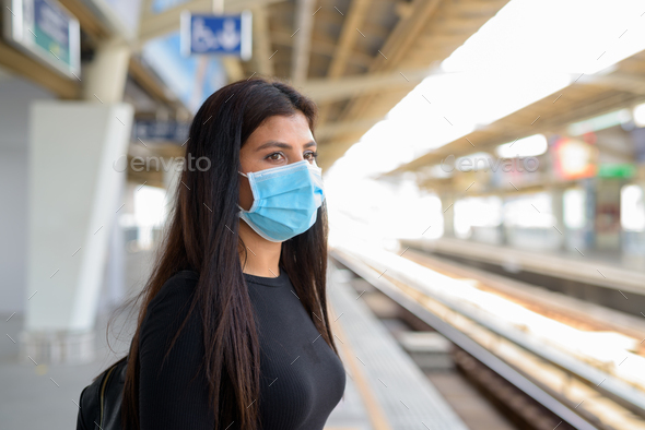 Young Indian woman with mask for protection from corona virus outbreak waiting at the sky train
