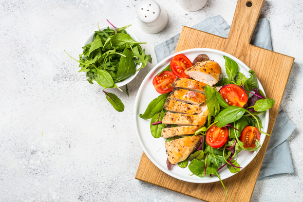 Grilled chicken fillet at wooden cutting board with vegetables Stock Photo  by Nadianb