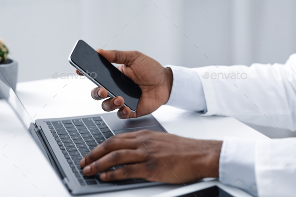 Close up of doc hands holding phone and using laptop