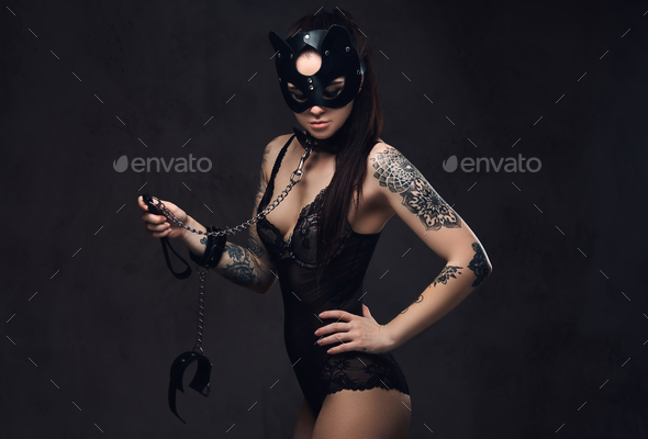 Sexy woman wearing black lingerie in BDSM cat leather mask and accessories posing on dark