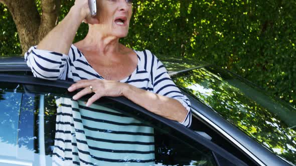 Senior woman talking on mobile phone near car alt