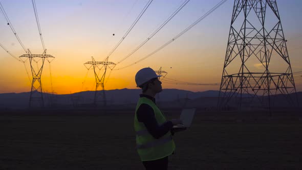 Engineer working in front of power lines at sunset. alt