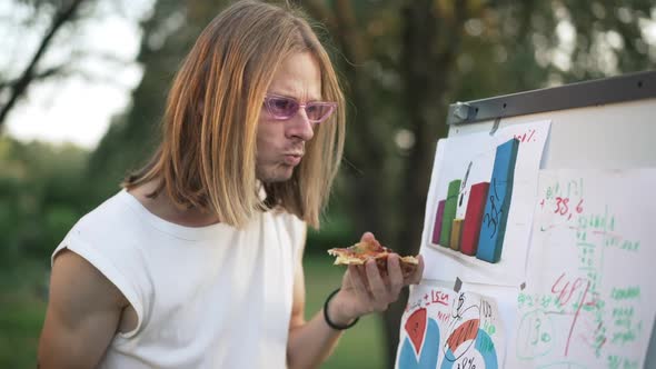 Focused Male Young Startuper Eating Pizza Writing on Whiteboard Outdoors in Summer Spring Park alt