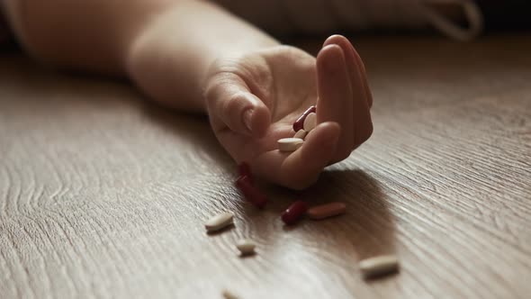 Woman Lying Unconscious on the Floor with Capsules in Her Hand alt