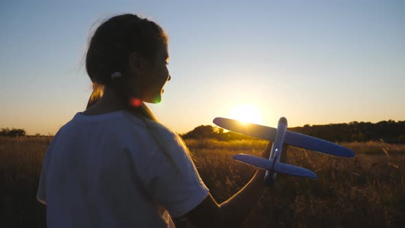 Little Smiling Girl Plays with Plane Going Along Grass Field at Sunset Time alt