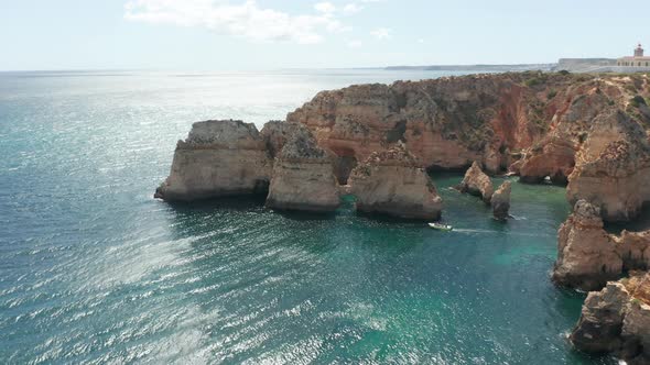 Beautiful aerial of small motor boat moving over stunning blue sea between high cliffs alt