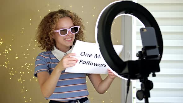 Cheerful Girl Blogger Shows a Poster with One Million Subscribers to the Camera