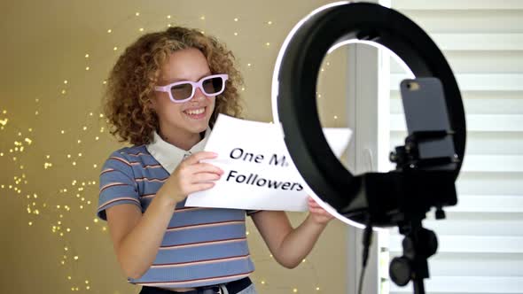 Cheerful Girl Blogger Shows a Poster with One Million Subscribers to the Camera alt