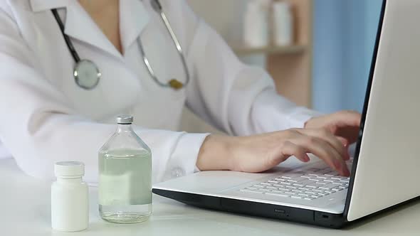 Doctor Typing Report on Laptop Keyboard, Checking Information on Pharmacy Bottle