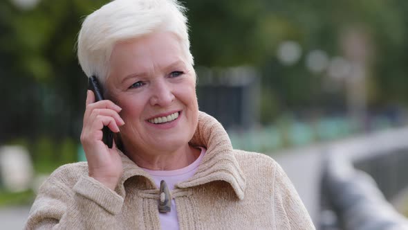 Happy Middle Aged Senior Caucasian Woman Grandma Enjoying Weekend Outdoors in City Park Talking on alt